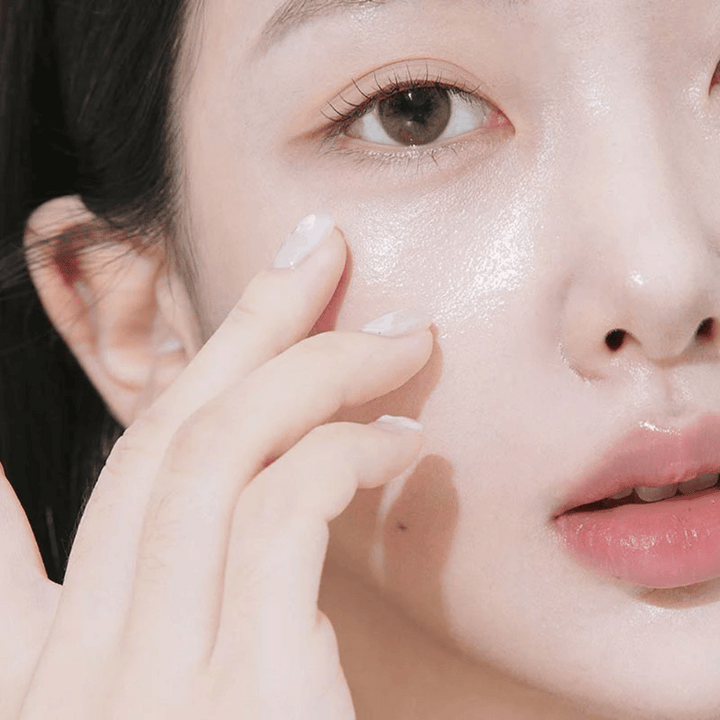 Närbild på en kvinna som applicerar ögonkräm under ögat med fingertopparna. Huden ser återfuktad, glansig och vårdad ut med naturlig lyster.