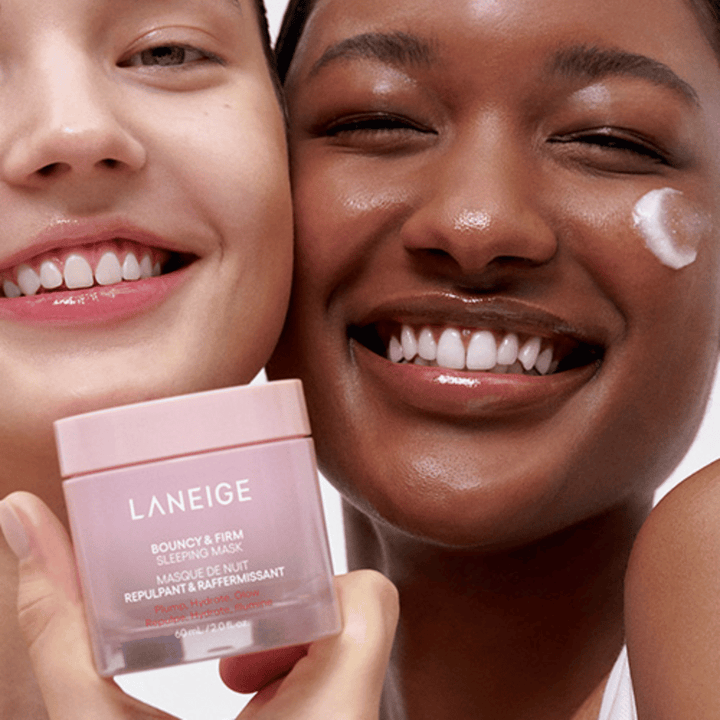 Två personer ler och håller i Laneige Bouncy & Firm Sleeping Mask. Den ena har applicerat masken på sin kind, och produkten syns tydligt i deras händer. Masken är i en rosa burk och marknadsförs som "Plump, Hydrate, Glow.