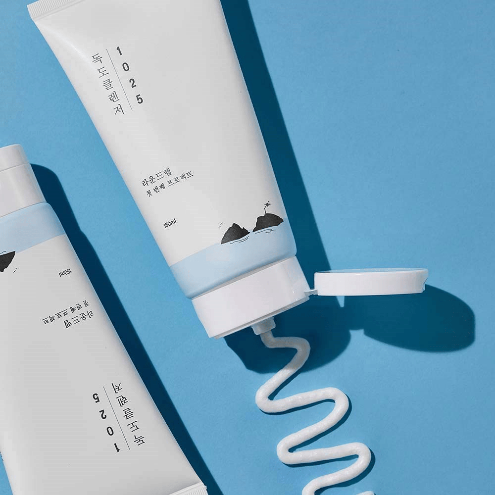Two tubes of 1025 Dokdo Cleanser on a blue background, one with an open cap and a wavy strand of cleanser squeezed out.