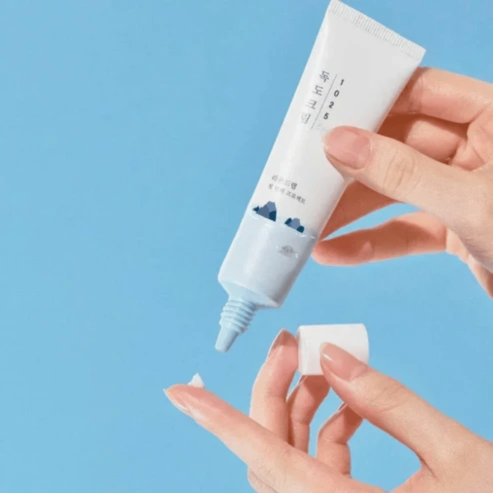 Round Lab 1025 Dokdo Eye Cream tube with a light cream applied to the fingertip for gentle care of sensitive skin around the eyes