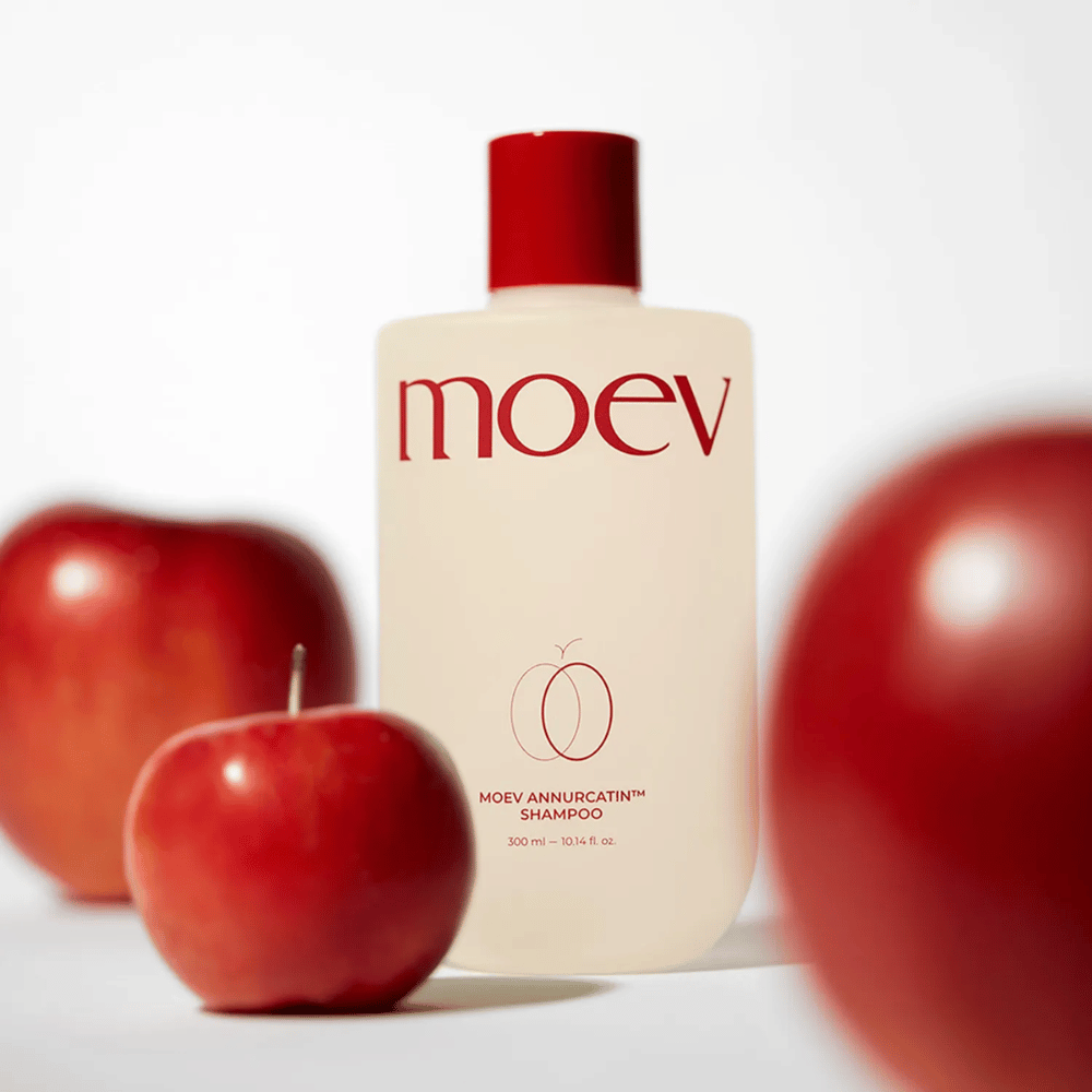 MOEV Annurcatin Shampoo placed among red apples – inspired by the antioxidants of the Annurca apple that provide stronger, healthier, and shinier hair.