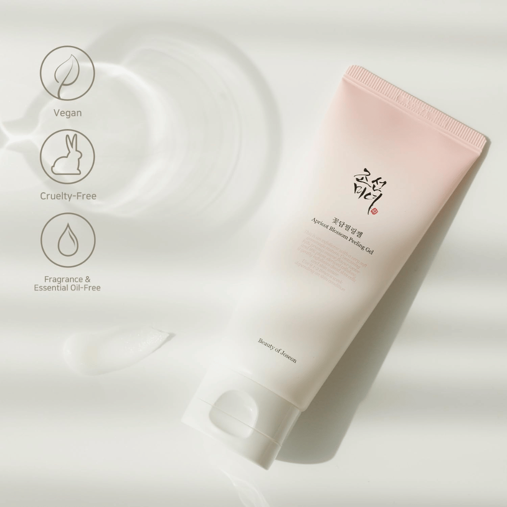 A tube with Apricot Blossom Peeling Gel lies on a reflective surface with icons indicating that the product is vegan, animal-friendly, and free from fragrance and essential oils.