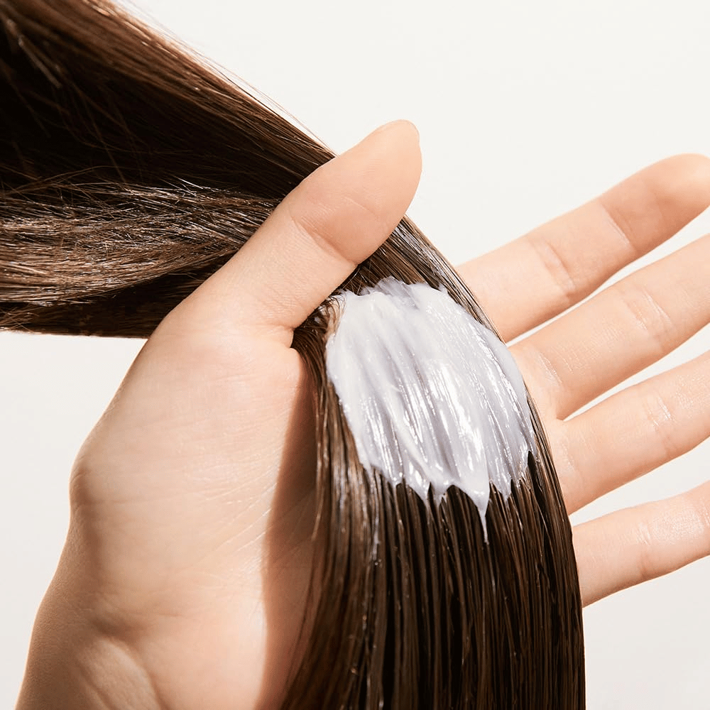 Hand applicerar Nature Republic Argan Essential Moisture Repairing Hair Mask i vått hår – återfuktande inpackning som stärker och mjukgör håret.