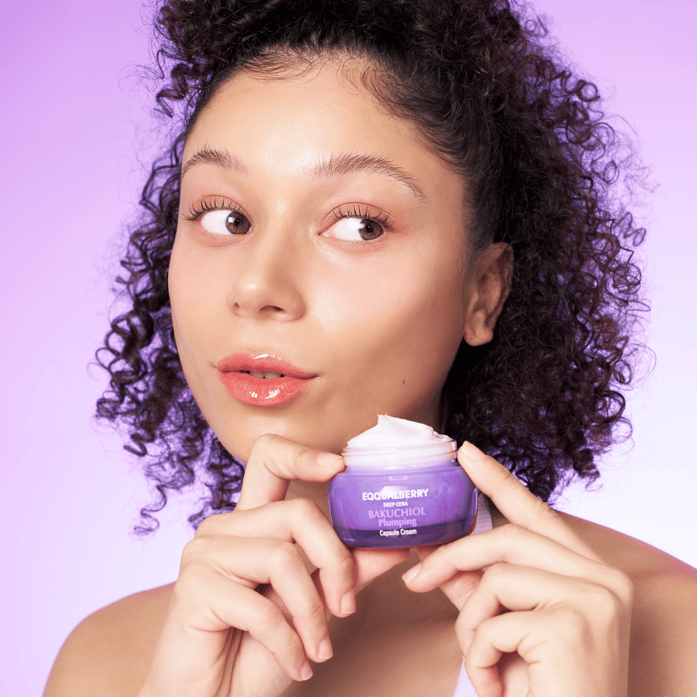 Kvinna håller EQQUALBERRY Bakuchiol Plumping Capsule Cream i handen och visar upp sin återfuktade, glödande hud mot en lila bakgrund.
