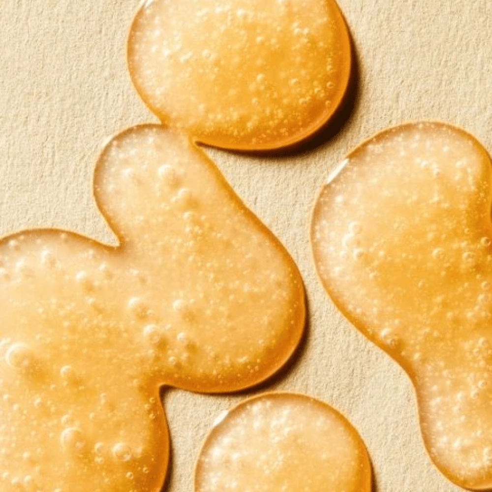 Texture image showing the serum’s golden formula with small bubbles and a light gel-like consistency.