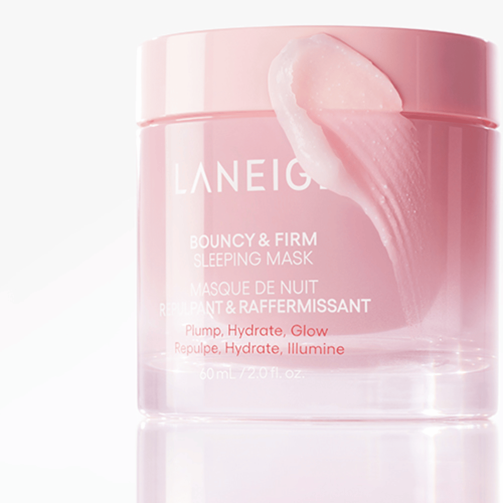 Close-up of Laneige Bouncy & Firm Sleeping Mask in a pink jar, with some of the mask applied to the edge of the lid. The product is intended to provide plumpness, hydration, and glow. The jar holds 60 ml and has the text "Plump, Hydrate, Glow."