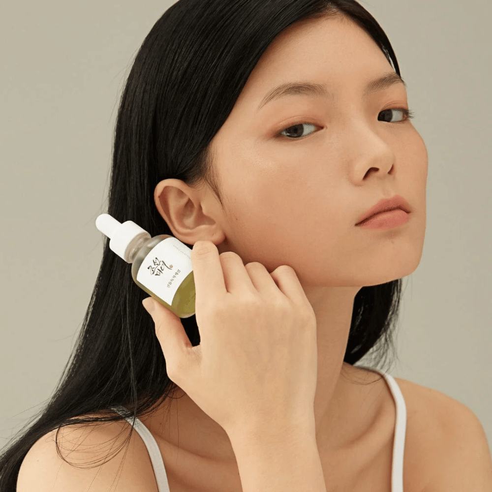 Model holds Beauty of Joseon Calming Serum by the cheek – green tea and panthenol that strengthens the skin barrier.
