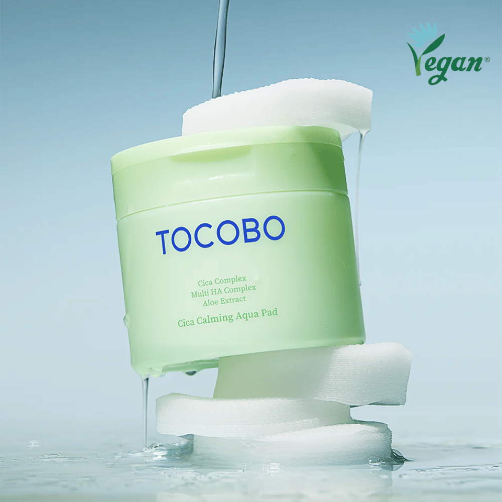 TOCOBO Cica Calming Aqua Pad placed among toner pads with flowing essence. The vegan symbol emphasizes the product's vegan formulation and skin-friendly profile.