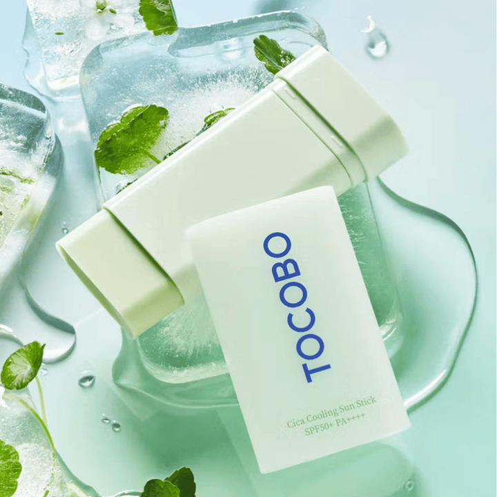 Tocobo Cica Cooling Sun Stick SPF50+ PA++++ på isbitar med gröna växtblad, vilket förmedlar en kylande och uppfriskande känsla.