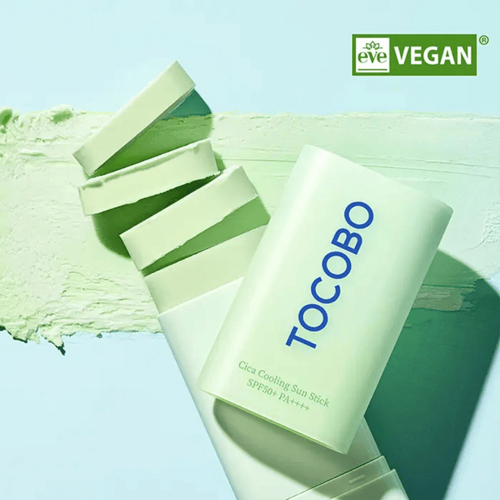 Tocobo Cica Cooling Sun Stick SPF50+ PA++++ i ljusgrön förpackning med veganmärkning (EVE VEGAN), liggande på ett lager av grönt solstift.