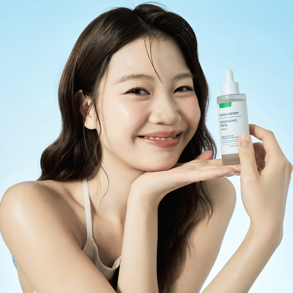 Smiling woman holding up Eqqualberry Swimming Pool Ampoule, a moisturizing skincare product, with both hands in front of a light blue background.