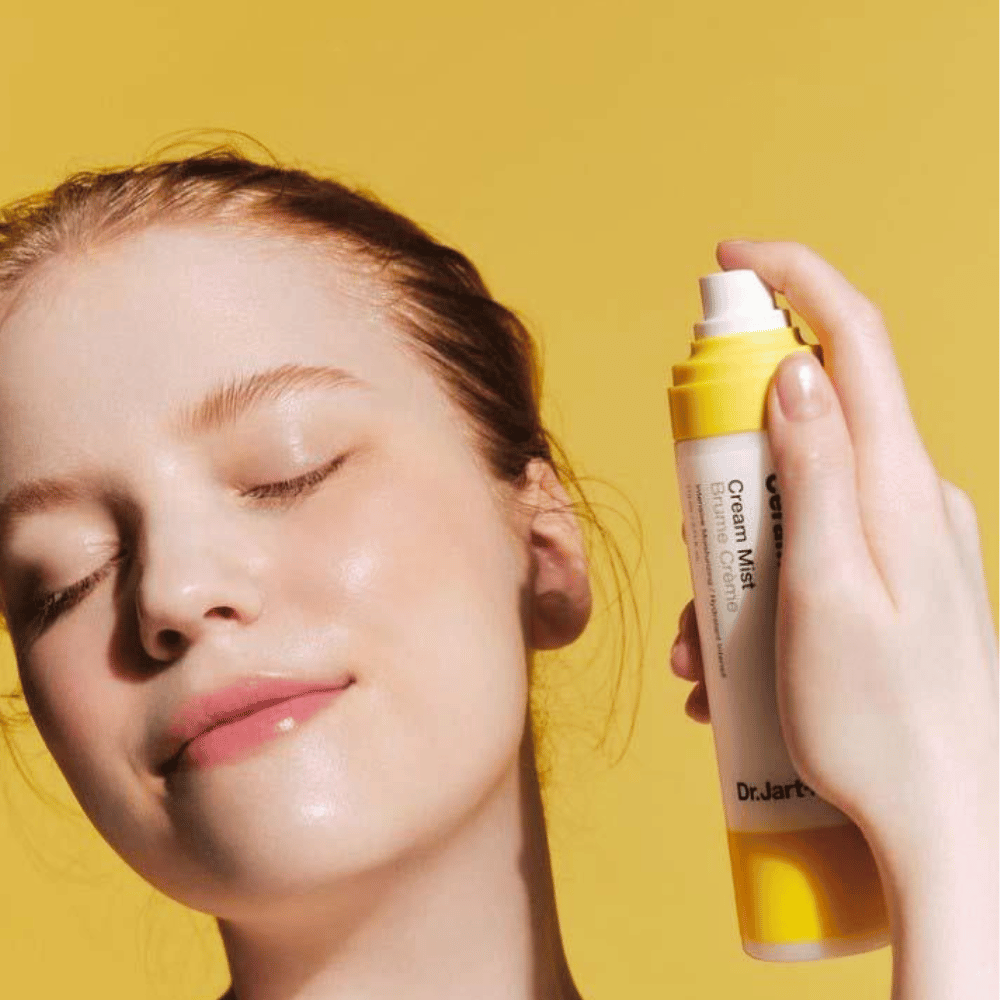 A woman holds a bottle of Dr. Jart+ Ceramidin Cream Mist 110ml to her face, promoting its moisture-boost benefits and vegan formulation.