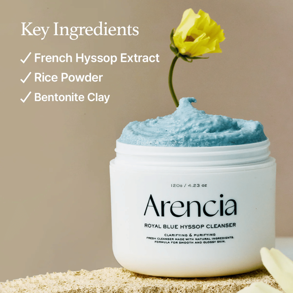 Image of the jar "Arencia Royal Blue Hyssop Cleanser" filled with blue cleansing cream. A yellow flower sticks out of the cream. The text in the image highlights three key ingredients: French Hyssop Extract, Rice Powder, and Bentonite Clay.