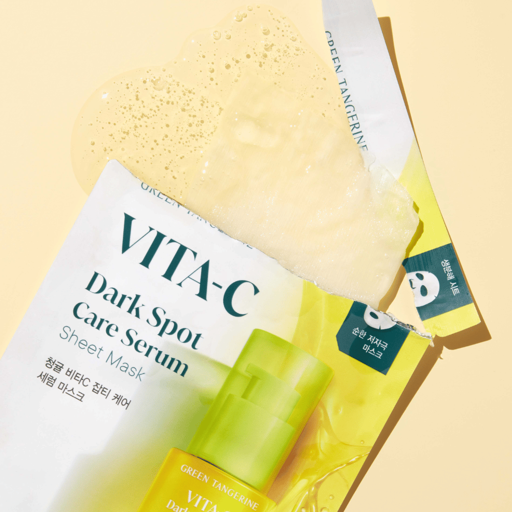 Opened packaging of VITA-C Dark Spot Care Serum Sheet mask with a face mask on top and a green serum bottle, all against a yellow background.
