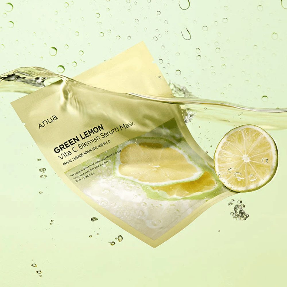 A vibrant image of Anua Green Lemon Vita C Blemish Serum Mask packaging with transparent water droplets and slices of green lemon around it. The packaging is partially covered by a stream of water on a light green background.