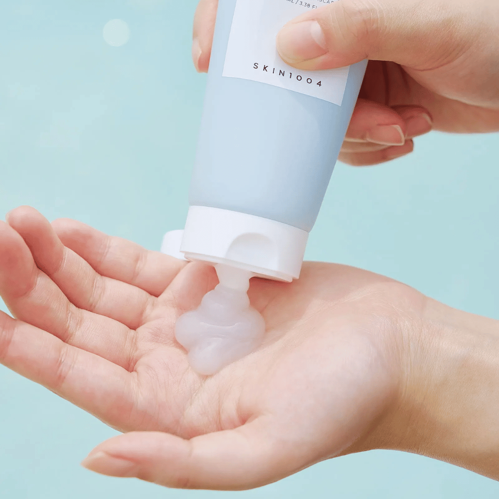 The image shows someone squeezing out a clear gel-like substance from a tube labeled "SKIN1004 Madagascar Centella Hyalu-Cica Sleeping Pack" containing 100 ml of product.