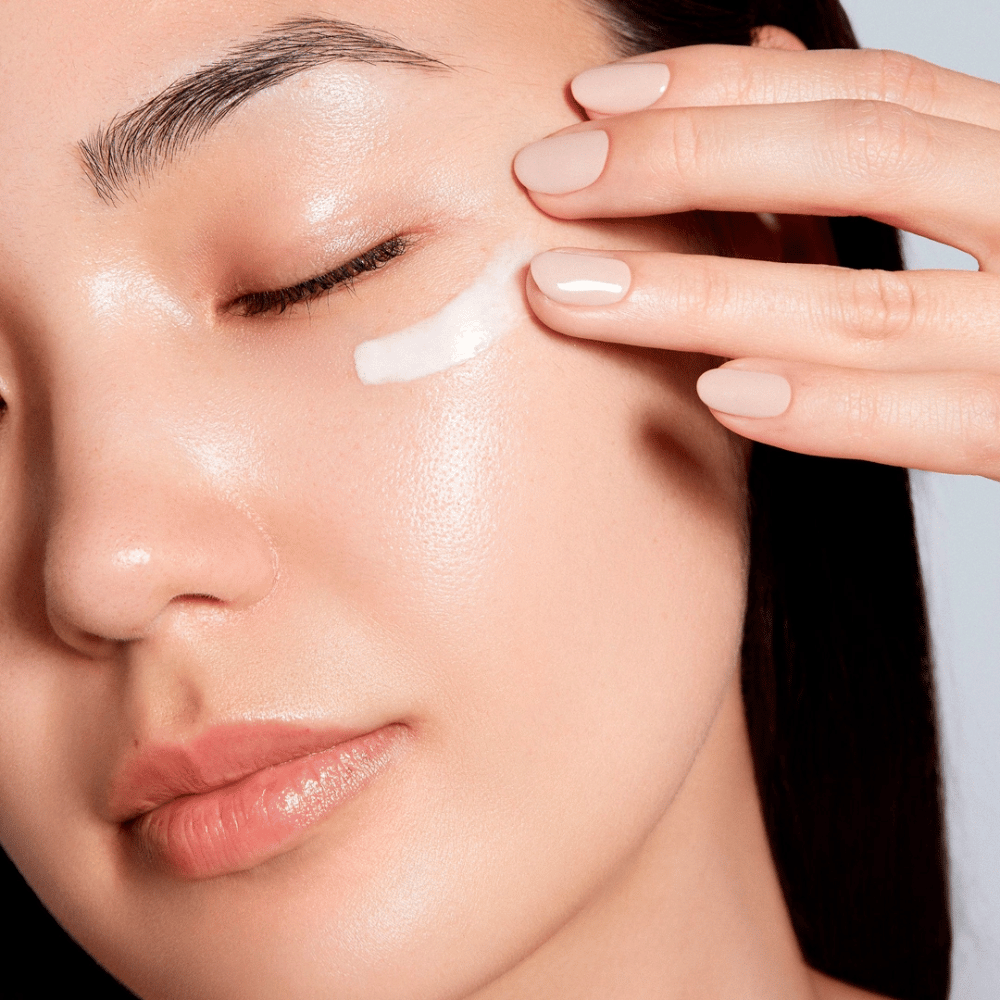 A woman carefully applies a white eye cream under her eye. Her skin looks radiant and hydrated, emphasizing the effect of the eye cream. This highlights the product as both moisturizing and suitable for the sensitive skin around the eyes.