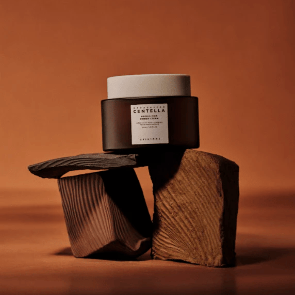 SKIN1004 Madagascar Centella Probio-Cica Enrich Cream in elegant brown glass jar on decorative wooden blocks – nourishing Korean face cream that strengthens the skin barrier.