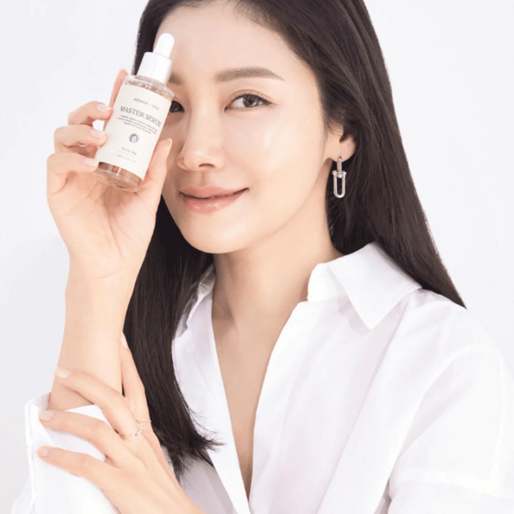 Smiling woman with long, dark hair and a white shirt holds up Mixsoon Master Serum next to her face. Her skin looks radiant and moisturized.
