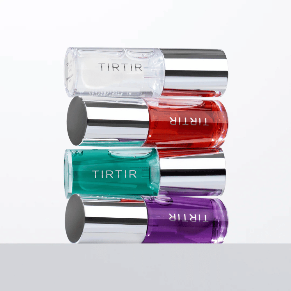 Four TIRTIR My Glow Lip Oil in different colors – transparent, red, green, and purple – stacked on top of each other with silver-colored caps against a white background.