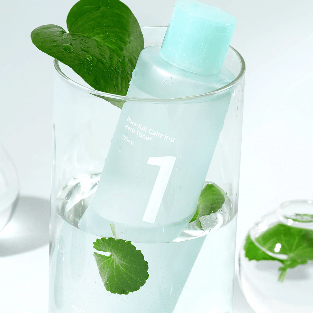 A bottle with No.1 Pure-Full Calming Herb Toner placed in a glass with water and green leaves. The bottle has a light blue cap and a label with the text "Pure-full Calming Herb Toner" and "300ml". The product looks fresh with water and greenery in the background, which gives a calming and natural feeling.