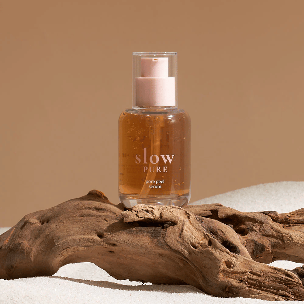 Slow Pure Pore Peel Serum placed on sand with wooden detail in the background, symbol of natural skincare.