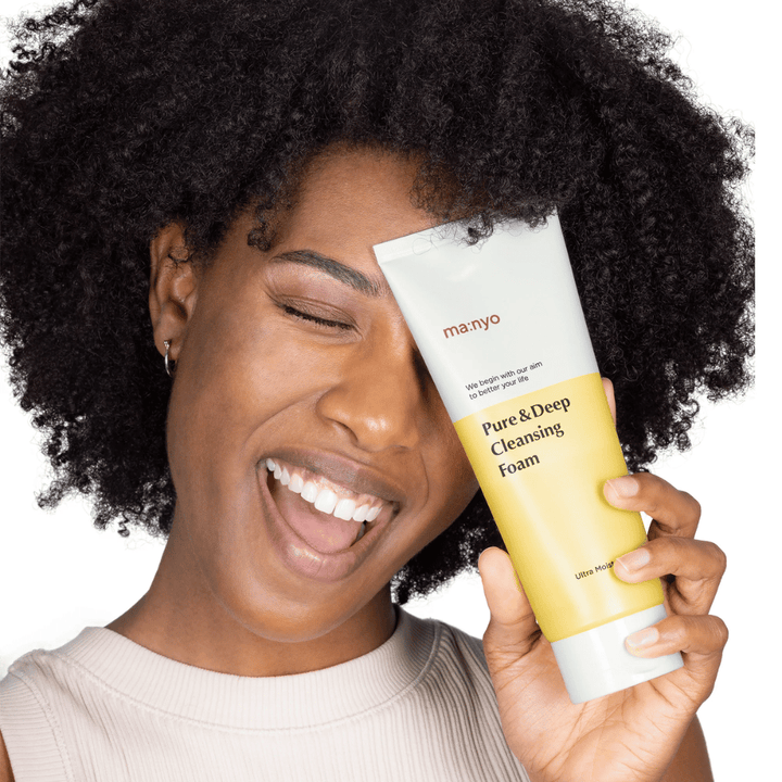 Woman with curly hair holding Ma:nyo Pure & Deep Cleansing Foam – a gentle Korean cleanser that effectively removes dirt and makeup without drying out the skin.