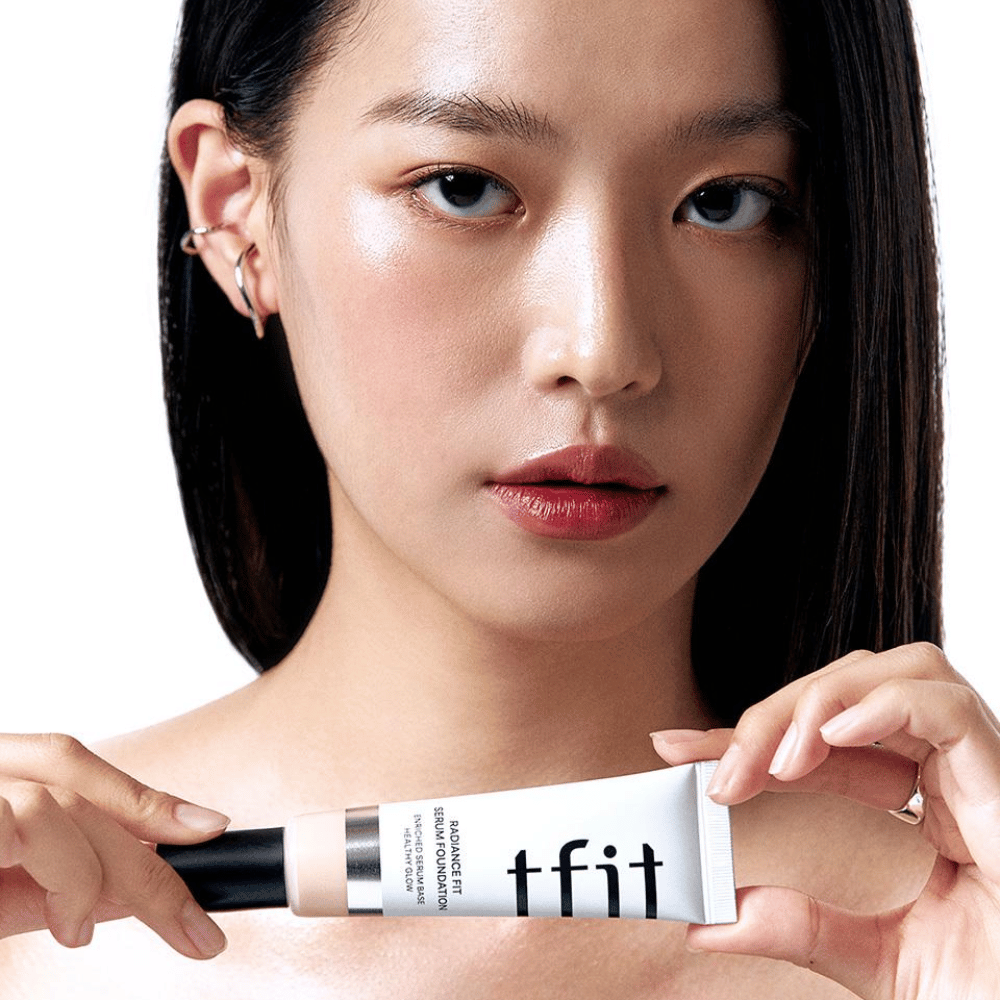 Model with glossy, smooth skin holding TFIT Radiance Fit Serum Foundation, highlighting the product's natural finish and glow.