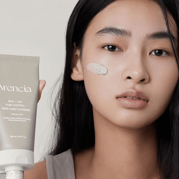 Model holding Arencia Rice + LHA Pore Control Rice Cake Cleanser with applied product on the cheek, illustrating mild yet effective pore cleansing for daily use.