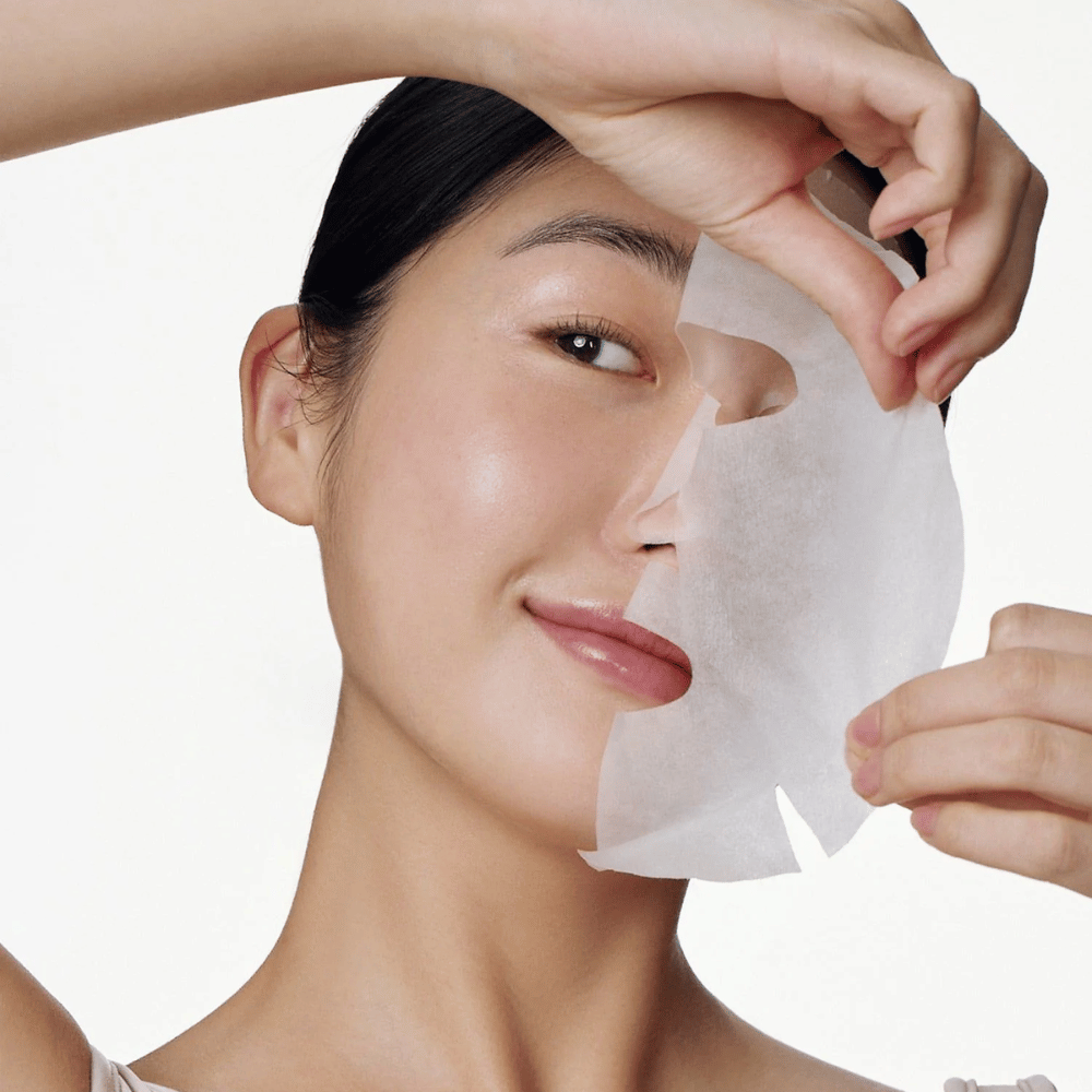 This image shows a person using a face mask, specifically "Galactomyces Glutathione Daily Mask" from Some By Mi. The mask brightens the skin and gives a radiant glow while nourishing and deeply hydrating the skin, thanks to ingredients like glutathione and vitamin C.