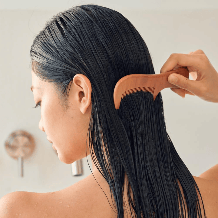 A person combs through long, wet hair with a wide-tooth comb after applying Heveblue Salmon Pullkeratin Centella Hair Treatment. Illustrates the detangling and softening effect for a smoother result.