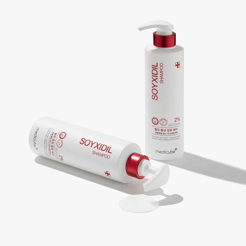 Two bottles of Medicube Soyxidil Shampoo in white and red design, one standing and one lying with spilled shampoo beside it.