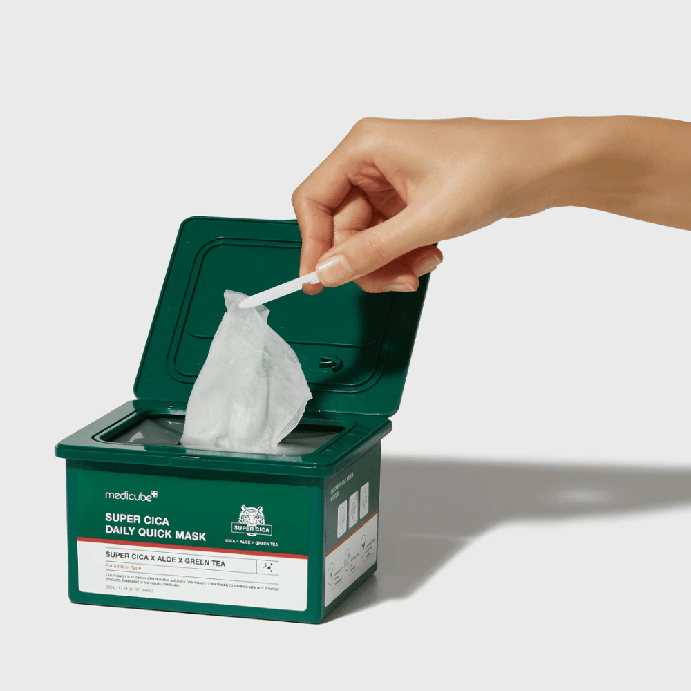 Grön behållare med öppet lock visar medicube Super Cica Daily Quick Mask. En hand drar upp en arkmask med medföljande pincett. Produkten innehåller Cica, aloe och grönt te, idealisk för snabb återfuktning och lugnande effekt.