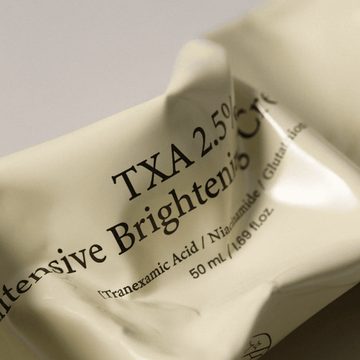 Close-up of AXIS - Y TXA 2.5% Intensive Brightening Cream where the soft and minimalist tube design is in focus. The image highlights the product name, Tranexamic Acid and Niacinamide, as well as the elegant beige packaging.